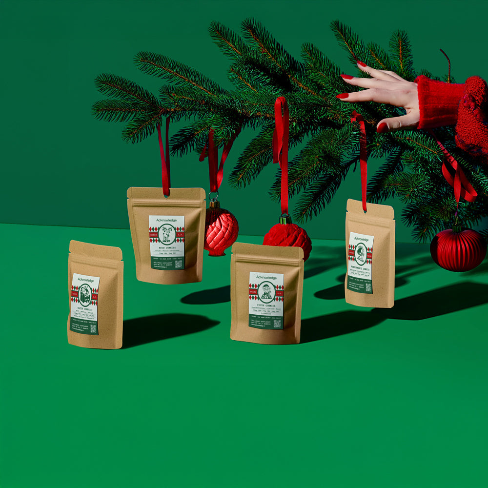 Acknowledge CBD Holiday gummies hanging from pine branches with red ornaments, promoting wellness gift ideas.