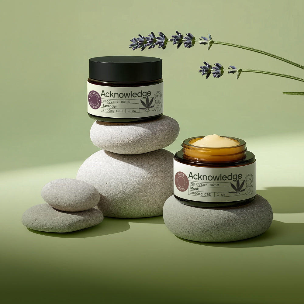 Acknowledge Recovery Balm jars with lavender and musk scents, displayed on spa stones for natural healing and relaxation.